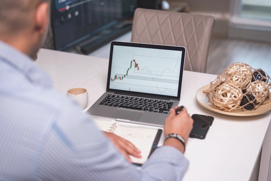 Osoba analizująca wykresy finansowe na laptopie z filiżanką kawy.